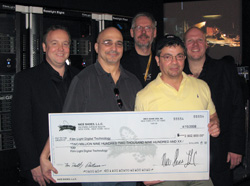 Five men smiling and posing together while holding a large ceremonial check in front of server equipment.