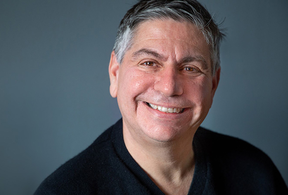 A middle-aged man with salt-and-pepper hair smiling against a gray background.