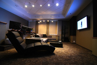 A dark media room featuring a large wall-mounted television, a sectional sofa, and a black recliner chair.