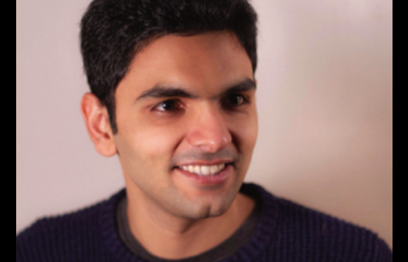 A smiling man with dark hair and a dark sweater looking slightly to the side.