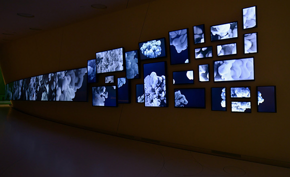 Multiple rectangular screens displaying blue and white cloud-like patterns arranged on a dark wall.