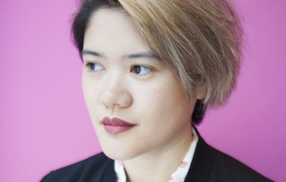 A person with short, side-swept blonde hair looking off-camera against a solid pink background.