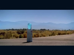 A white rectangular pillar stands in a dry field under a clear blue sky with mountains in the distance.