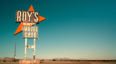 A large, weathered orange and white roadside sign for Roy's Motel and Cafe against a clear blue sky.