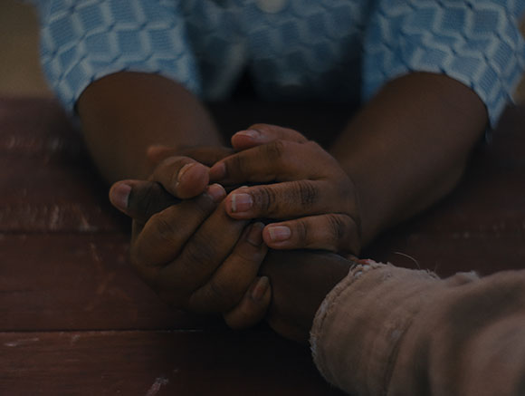 Close-up of two people's hands clasped together on a dark wooden surface.