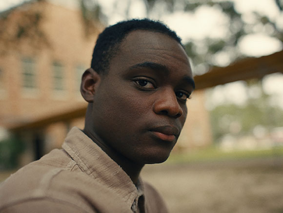 Close-up portrait of a young Black man looking directly at the camera with a neutral expression.