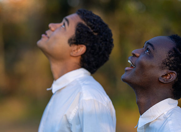 Two young men in white shirts looking up toward the sky with expressions of wonder.