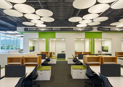 Modern office interior with white circular pendant lights, green walls, and rows of white desks with black chairs.