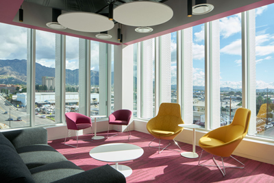Lounge with pink, yellow, and magenta chairs, a white coffee table, and floor-to-ceiling windows with a city view.