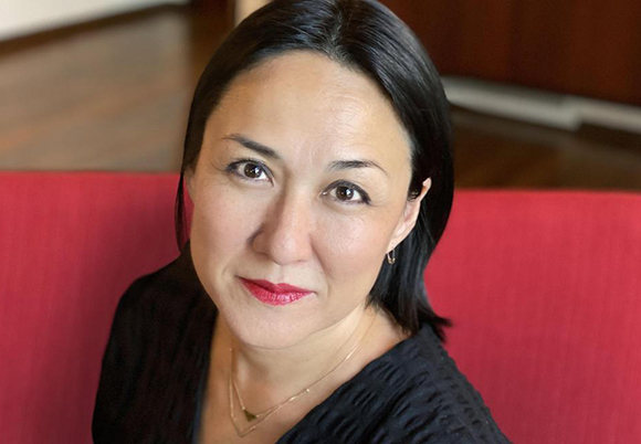 A woman with dark hair and a black top smiles slightly at the camera.