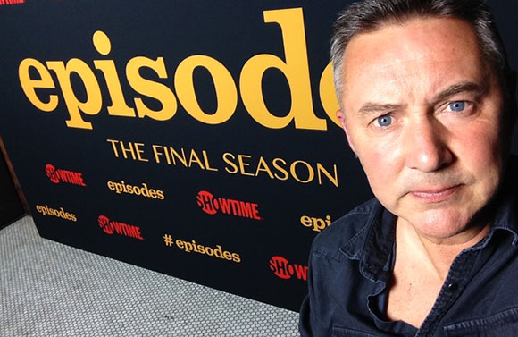 A man looking at the camera in front of a black backdrop with yellow 'episodes' text.