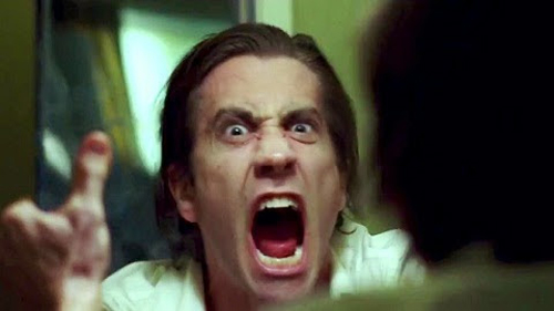 A man with dark hair and wide eyes screams with his mouth open while gesturing toward someone off-camera.