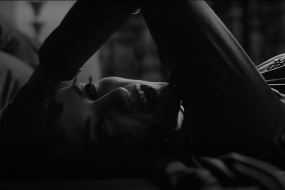Black and white close-up of a person lying down with their arms raised above their head.
