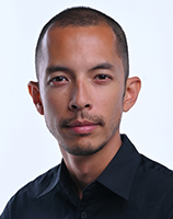 A man with short hair and a mustache wearing a dark collared shirt looks forward.