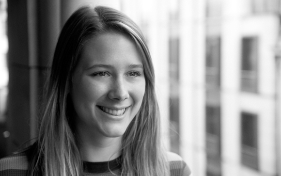 A smiling young woman with long hair looks slightly off-camera in a black and white portrait.