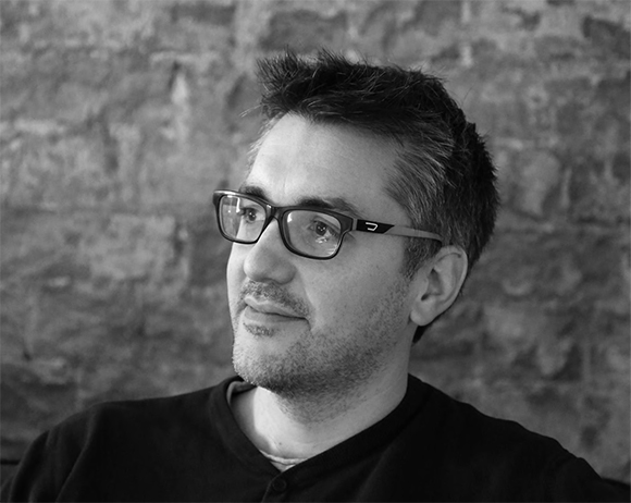 Black and white close-up portrait of a man with short hair and glasses looking slightly to the side.