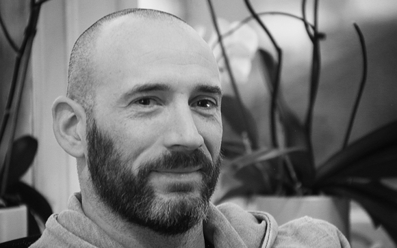 Black and white close-up portrait of a bald man with a beard looking toward the camera.