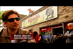 A man wearing sunglasses stands in front of a storefront labeled Patrizia's Pork Store.