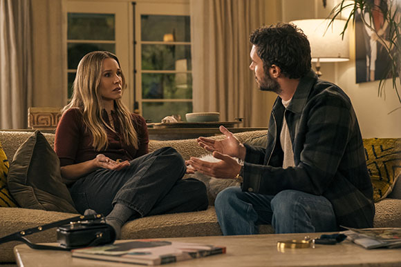 A man and a woman sit on a couch in a living room, engaged in an intense conversation.