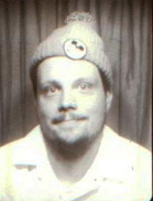 Black and white portrait of a man wearing a knit beanie with a pom-pom and a button.
