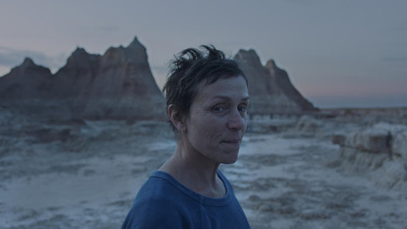 A woman in a blue shirt looks toward the camera against a backdrop of jagged rock formations at dusk.