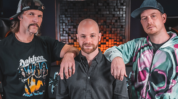 Three men pose for a portrait; one wears a Dokken t-shirt, one a dark button-down, and one a patterned jacket.