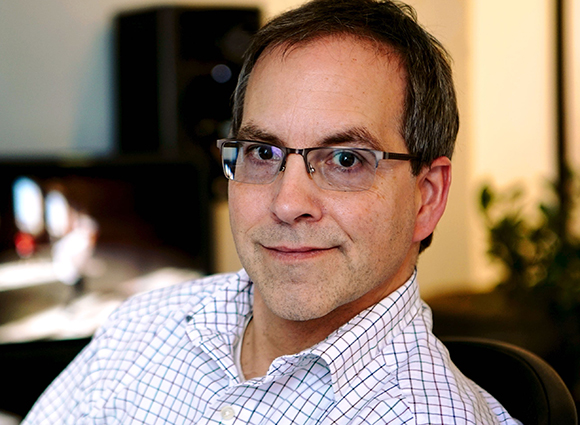 A man with short brown hair and glasses wearing a white and blue checkered shirt.