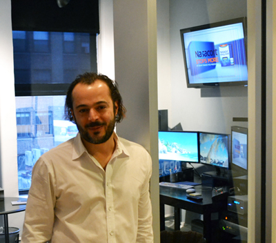 A man with dark hair and a beard wearing a white button-down shirt stands in an office.
