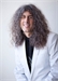 A smiling person with long, voluminous curly hair wearing a white blazer over a black shirt.