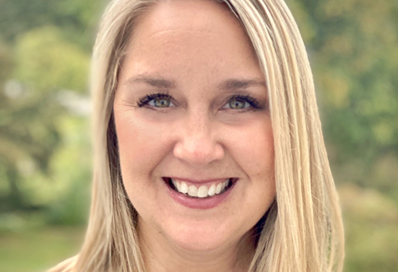 A smiling woman with long blonde hair and green eyes looking toward the camera.