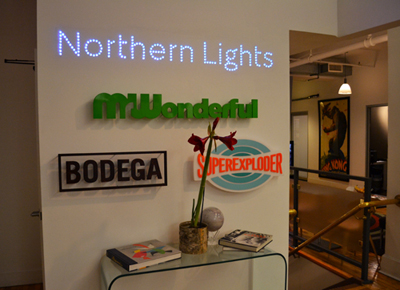 Three signs on a white wall: a lit LED 'Northern Lights', a green 'Wonderful', and a black 'Bodega'.