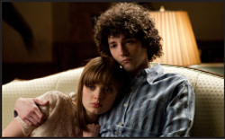 A young man with curly hair holds a young woman close as she rests her head on his chest.
