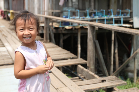 A young girl in a pink tank top smiles while standing on a weathered wooden boardwalk.