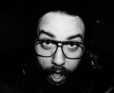 Black and white close-up of a man with glasses and a beard looking directly at the camera.