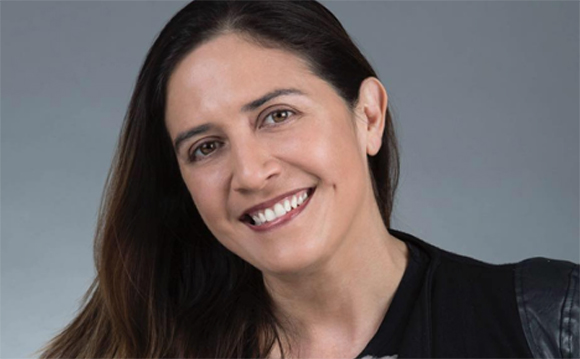 A smiling woman with long dark hair looking toward the camera against a gray background.