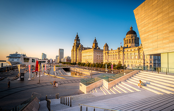 Historic waterfront buildings and a large cruise ship under a clear blue sky at sunset.