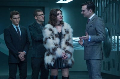 Four people in formal clothing stand in a dark, modern room, including a woman in a white fur coat.