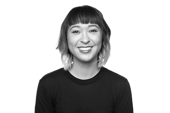 A smiling woman with short hair and bangs wearing a dark t-shirt.