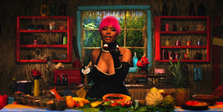 A woman with short pink hair wearing a black outfit, standing behind a table of tropical fruit.