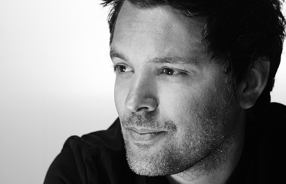 Black and white close-up portrait of a man with short dark hair and light stubble looking off-camera.