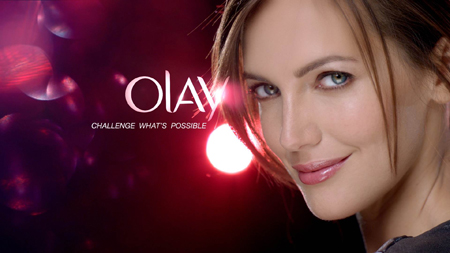 A woman smiling against a dark pink bokeh background with the Olay logo and text.