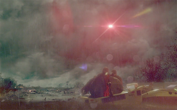A bright red light pierces through heavy fog and mist over a dark, hazy landscape.