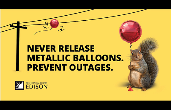 A squirrel holds a red metallic balloon near power lines, with a red balloon stuck on a wire in the background.