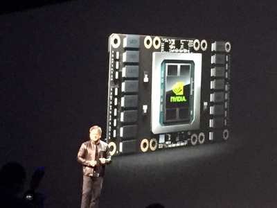 A man in a leather jacket stands on a stage presenting a large NVIDIA chip with the NVIDIA logo on it.