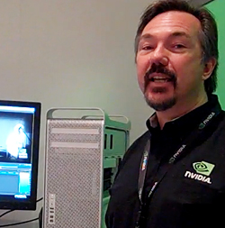 A man with a goatee wearing a black NVIDIA shirt stands next to a computer monitor and a server tower.