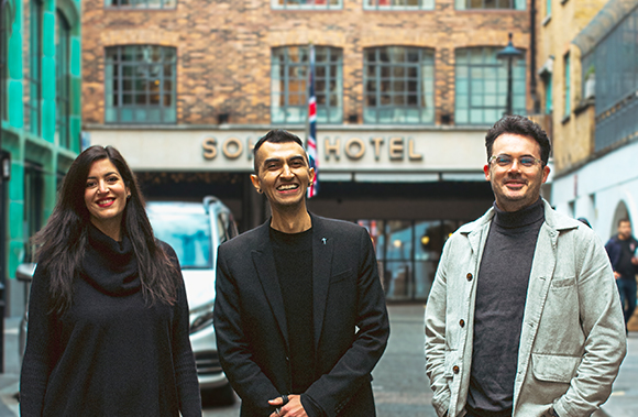 Three smiling people standing on a city street in front of a brick hotel building.