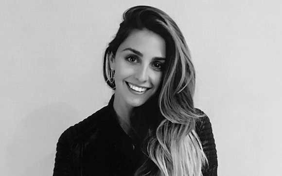 A smiling woman with long, wavy hair wearing large hoop earrings and a dark jacket.