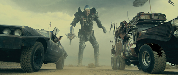 A massive armored figure stands in a desert between a black car and a large, rugged truck.