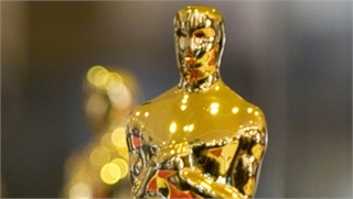 A close-up shot of a shiny, gold-colored humanoid trophy statue against a blurred background.