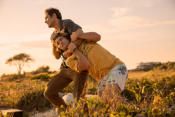 Two men engage in a wrestling match in a grassy field during a golden sunset.